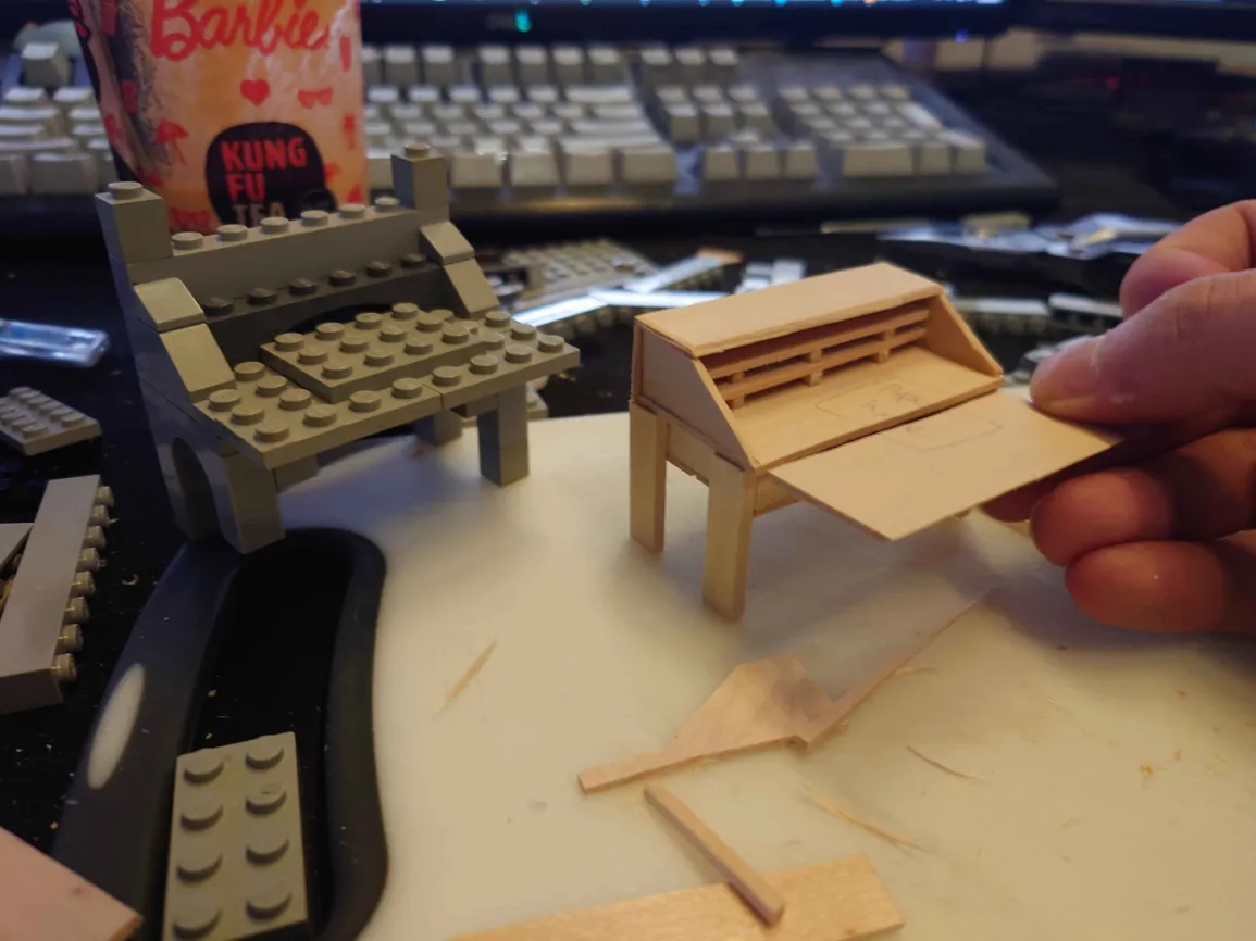 a small lego writing desk, next to an unpainted wooden version of approximate size and shape.